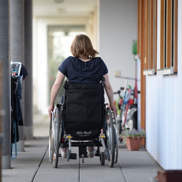 Eine Rollstuhlfahrerin fährt in einer Wohnanlage zu ihrer Wohnung.