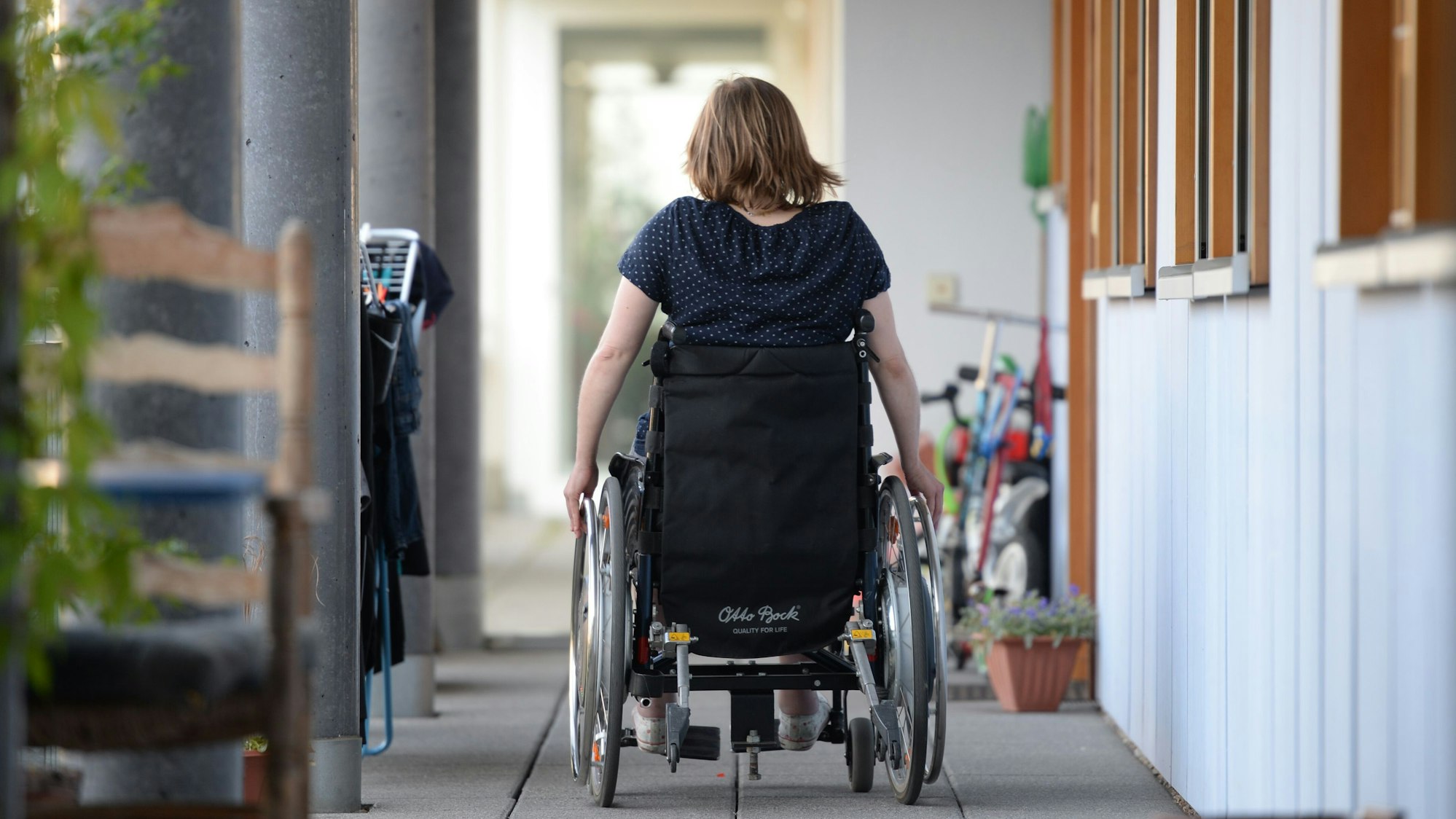 Eine Rollstuhlfahrerin fährt in einer Wohnanlage zu ihrer Wohnung.