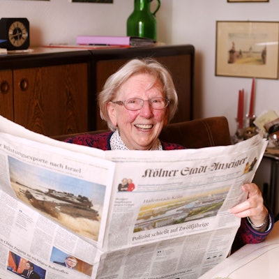 Margot Schoenniger (94) hält den „Kölner Stadt-Anzeiger“ in den Händen und lacht in die Kamera.