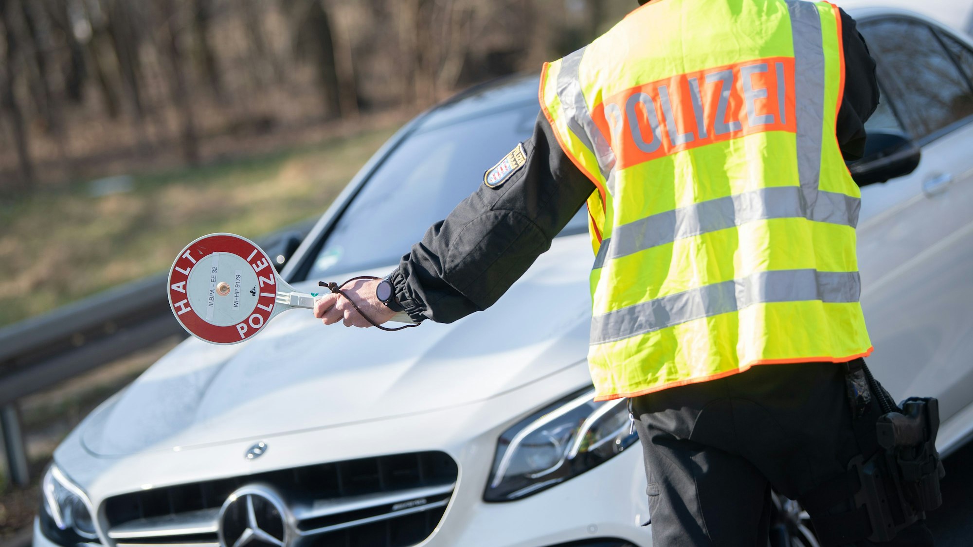 Ein Polizist hält einen Autofahrer mit einer „Halt Polizei“-Kelle an.