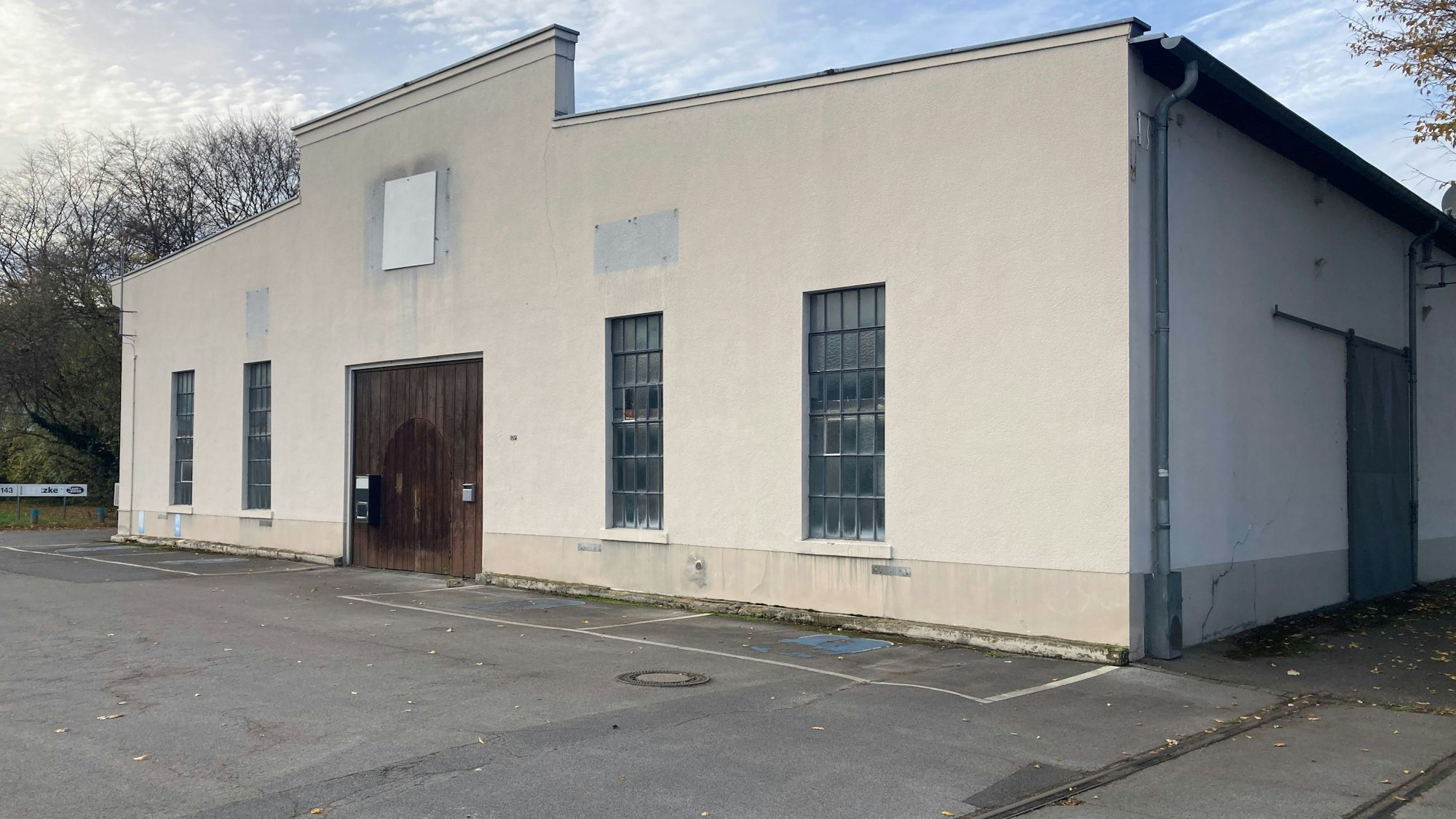 Eine weiß verputzte Halle aus Beton hat eine große Holztür und rechteckige Fenster.