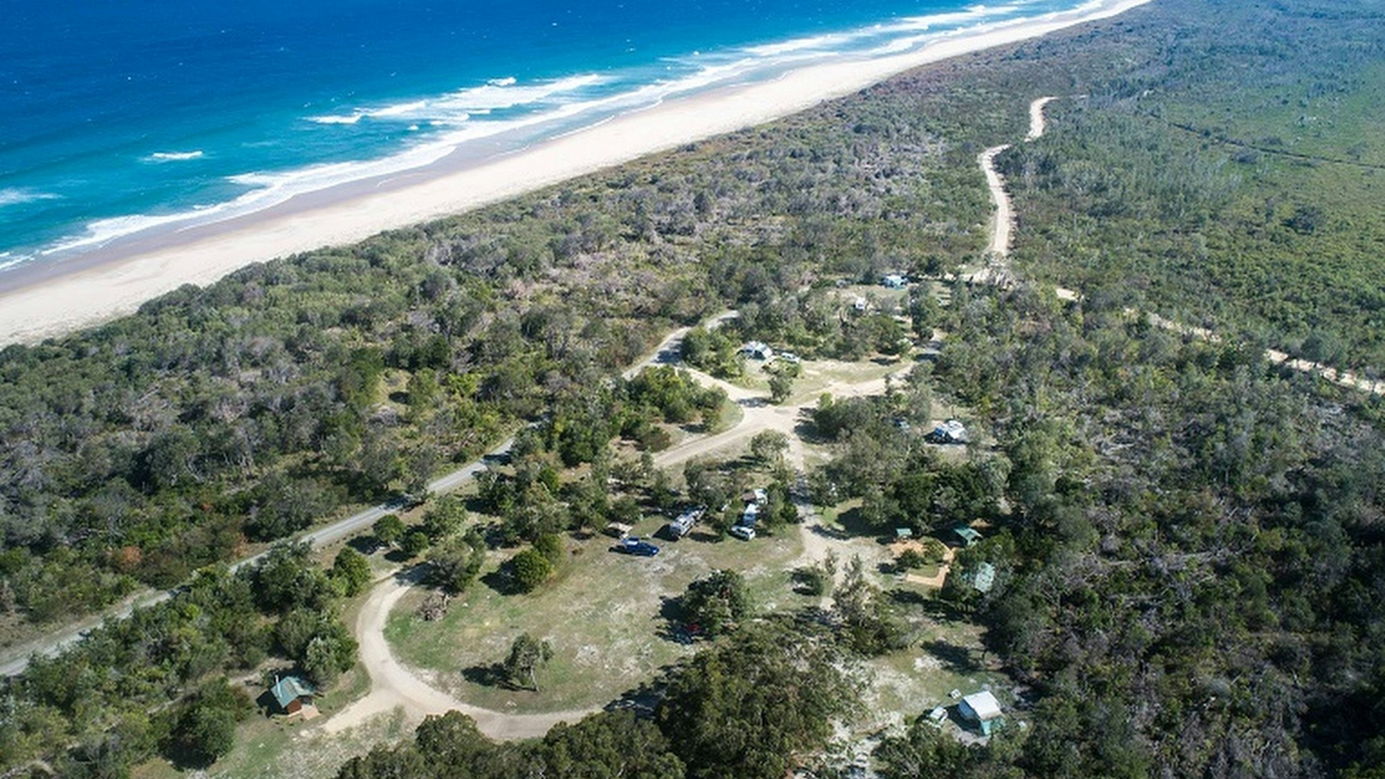 Luftaufnahme von Kylies Strand NSW mit Küste, Meer und einem bewaldeten Campingplatz