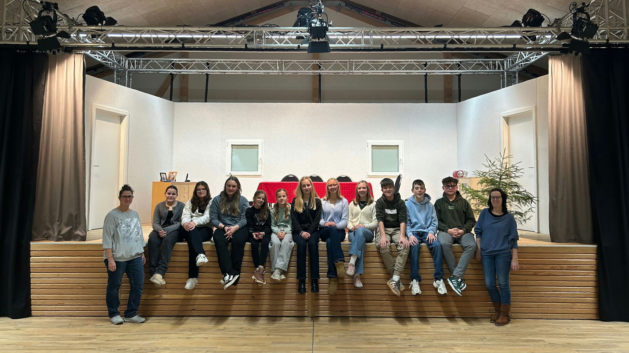Die Mittglieder der Jugendgruppe des Theatervereins sitzen in einer Reihe am Bühnenrand.