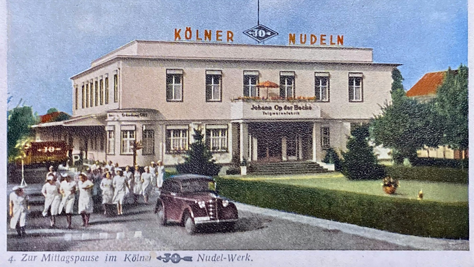 Frauen in weißen Kleidern und ein Auto stehen vor einem stattlichen Gebäude, auf dem der Schriftzug „Kölner JO Nudeln“ steht.