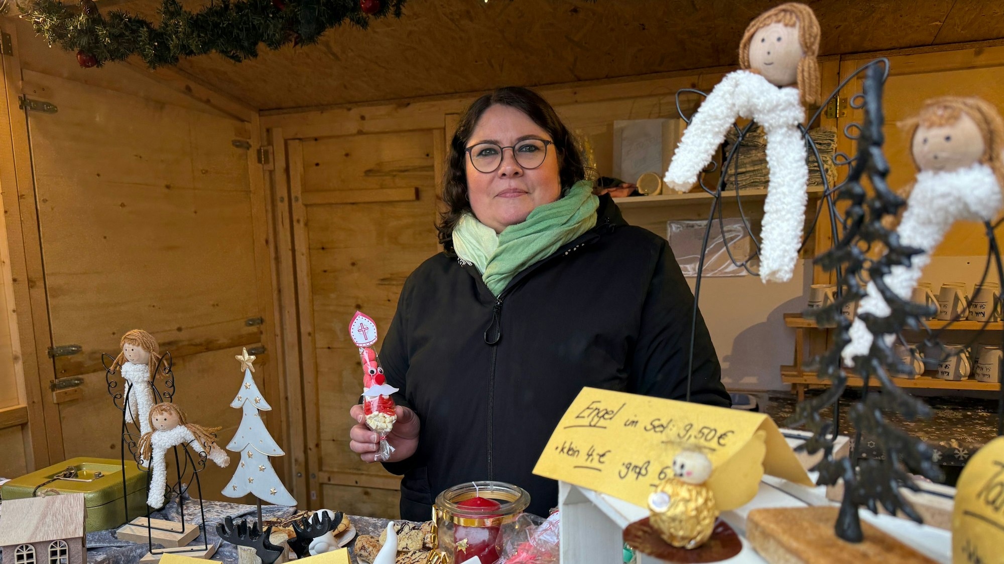 Eine Frau steht hinter einem Verkaufsstand mit Dekoartikeln auf einem Adventsmarkt.