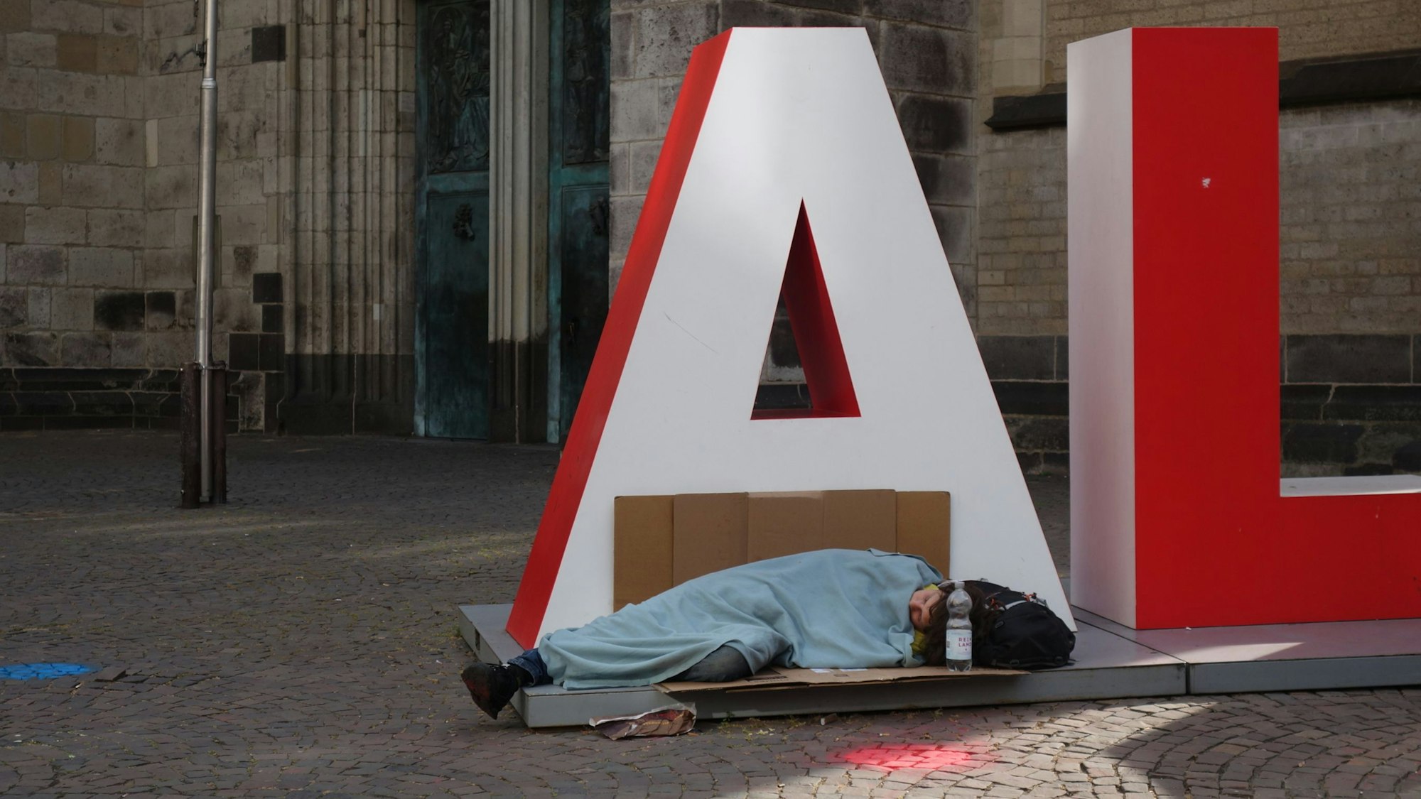 Eine obdachlose Frau schläft auf Pappe auf dem Alaaf-Schriftzug.