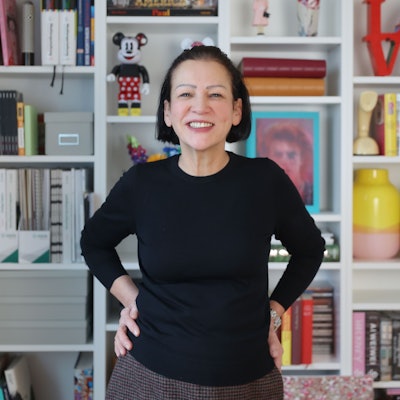 Claudia Malzkorn, Inhaberin der Kölner Kreativagentur Malzkorn, steht vor einem Regal mit bunten Design-Gegenständen und Büchern