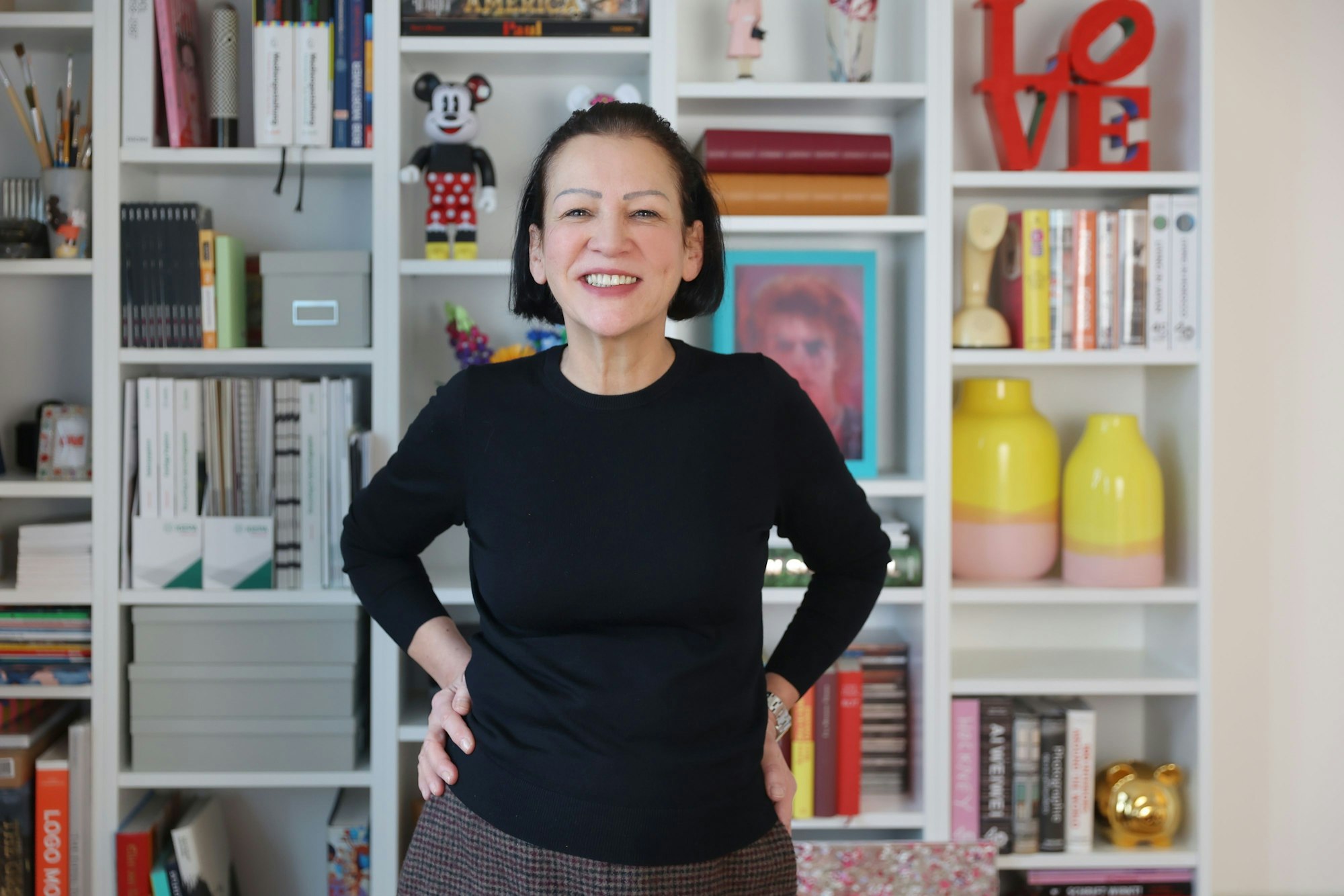 Claudia Malzkorn, Inhaberin der Kölner Kreativagentur Malzkorn, steht vor einem Regal mit bunten Design-Gegenständen und Büchern