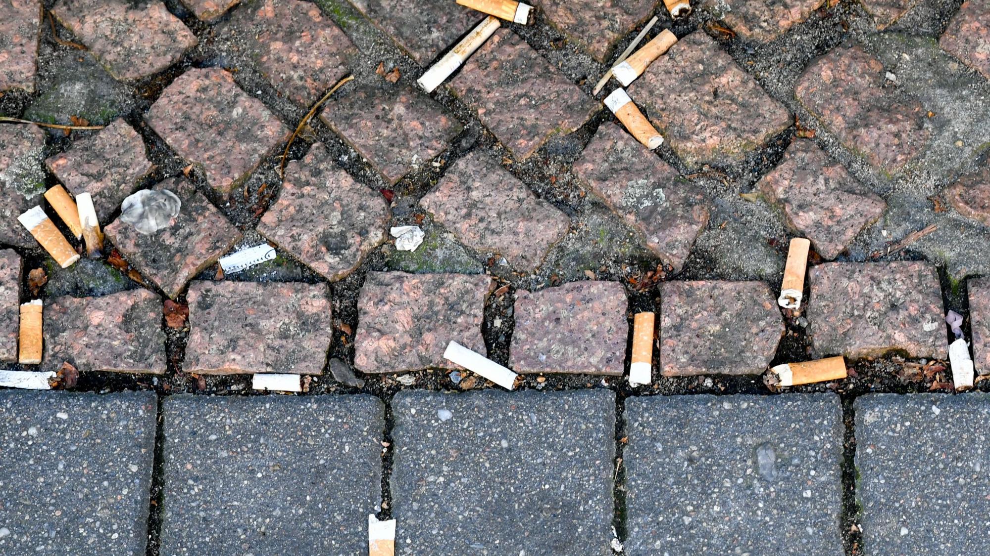 Zahlreiche auf den Boden geworfene Zigarettenstummel liegen auf dem Pflaster.