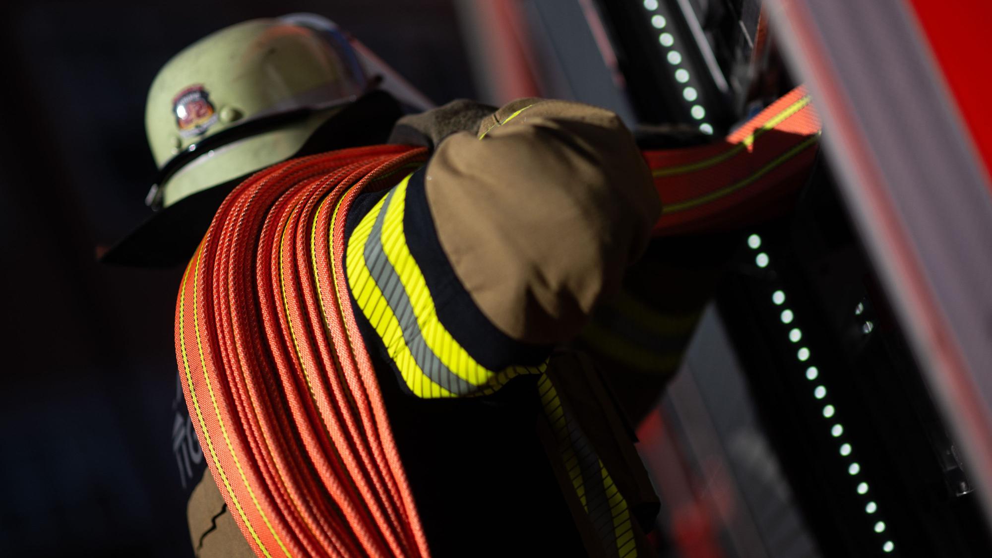 Eine Einsatzkraft der Feuerwehr nimmt einen Schlauch aus einem Einsatzfahrzeug der Feuerwehr. In Köln hat es in der Nacht gebrannt. (Symbolbild)