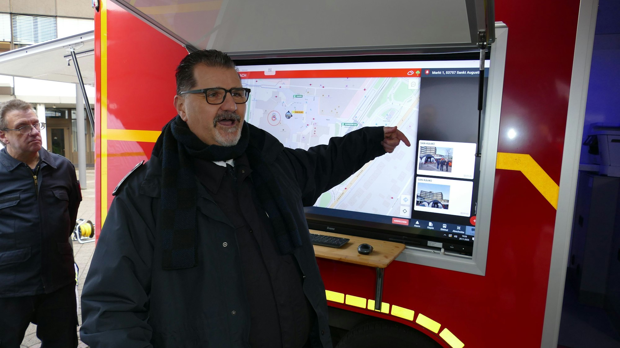 Ein Mann steht neben einem Fahrzeug und deutet auf einen Bildschirm.