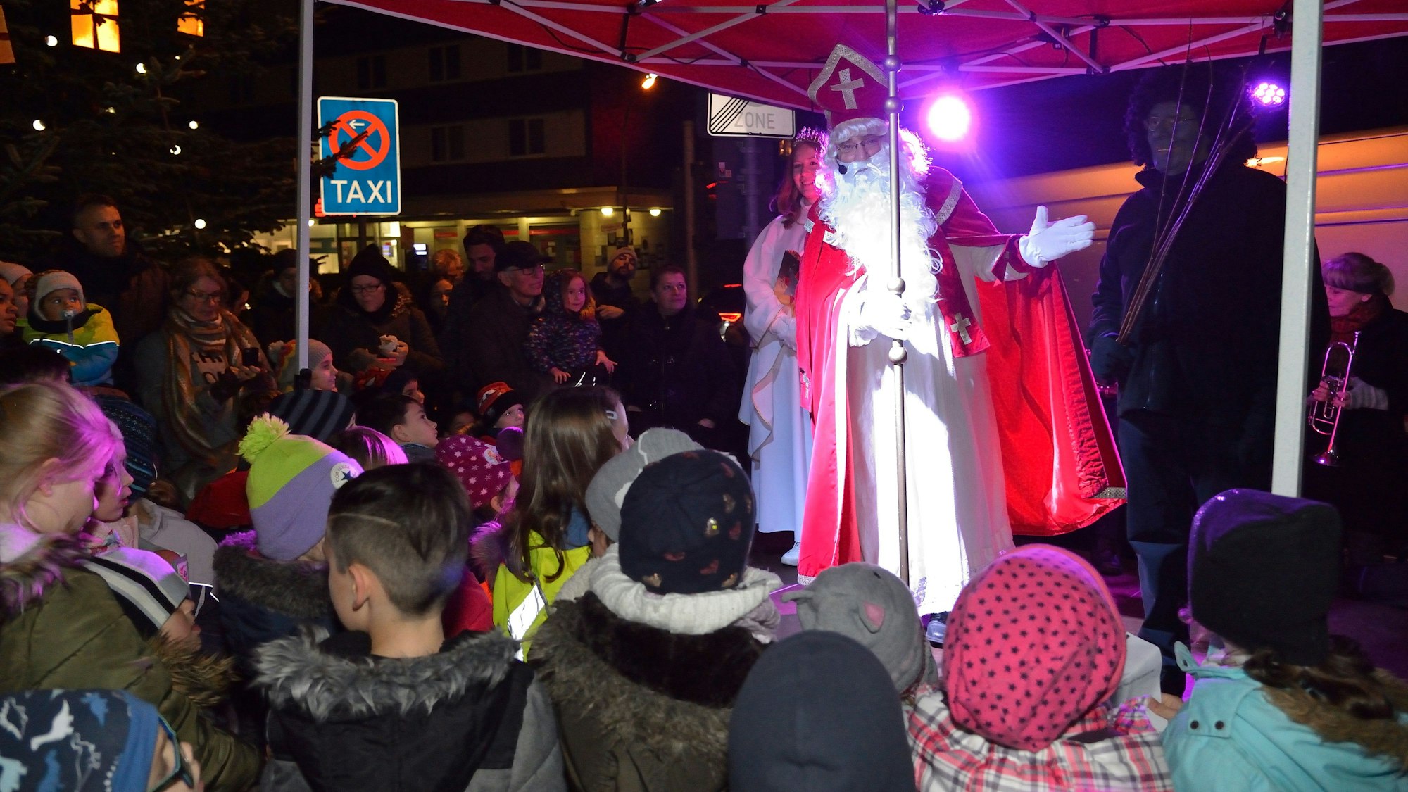 Der Nikolaus mit Engel und Knecht Ruprecht steht auf dem Nikolausmarkt vor St. Clemens in Bergisch Gladbach-Paffrath.