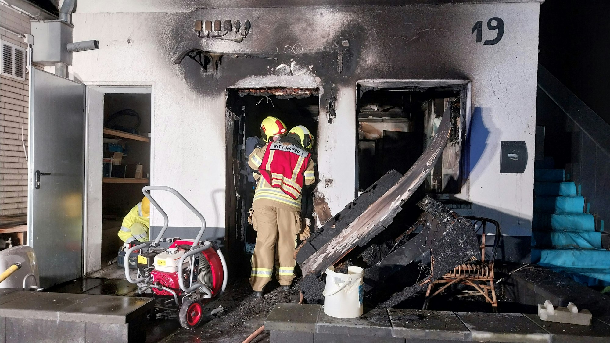 Einsatzkräfte der Feuerwehr vor einer ausgebrannten Wohnung.