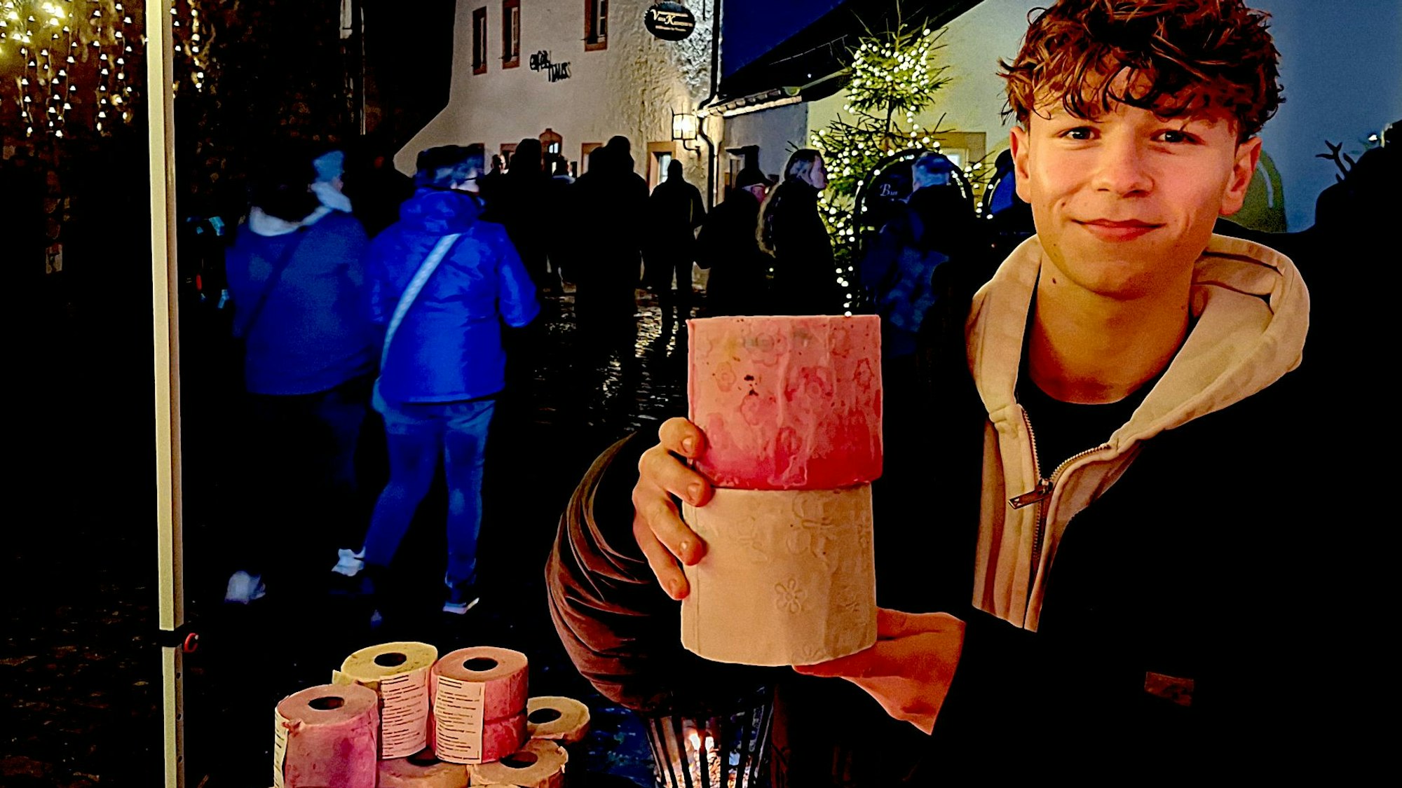 Ein junger Mann lächelt in die Kamera, in den Händen hat er die Klopapier-Fackeln, die er verkauft.
