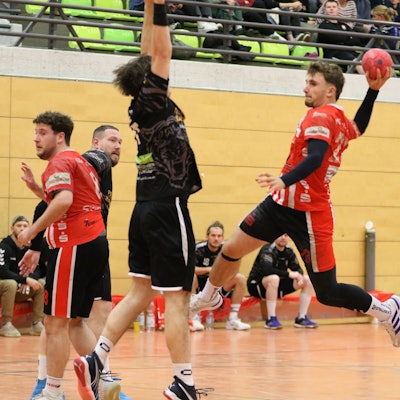 Schreiber ist zum Sprungwurf hochgestiegen. Ein Abwehrspieler versucht, den Ball zu blocken.