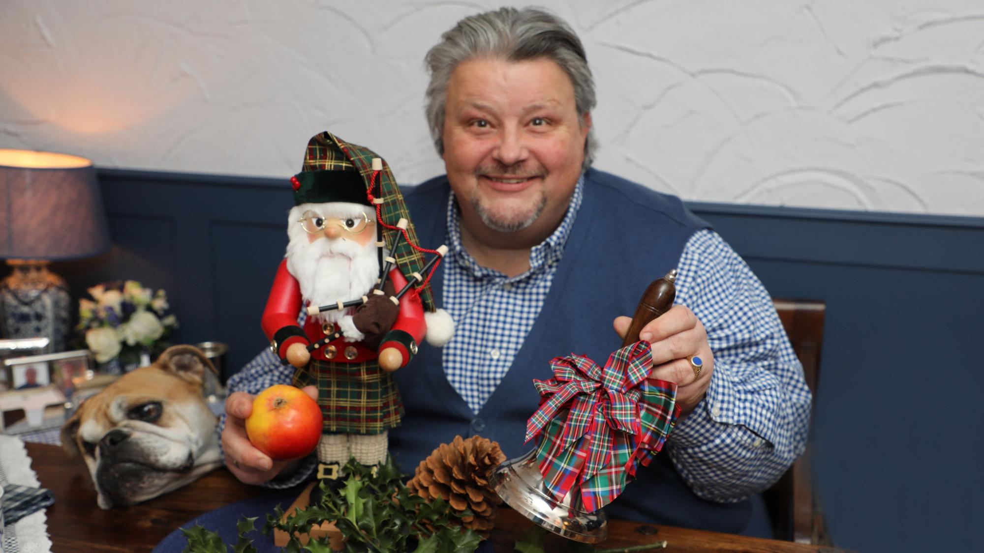 Ein Mann hat eine Glocke und einen Apfel in der Hand und lächelt.