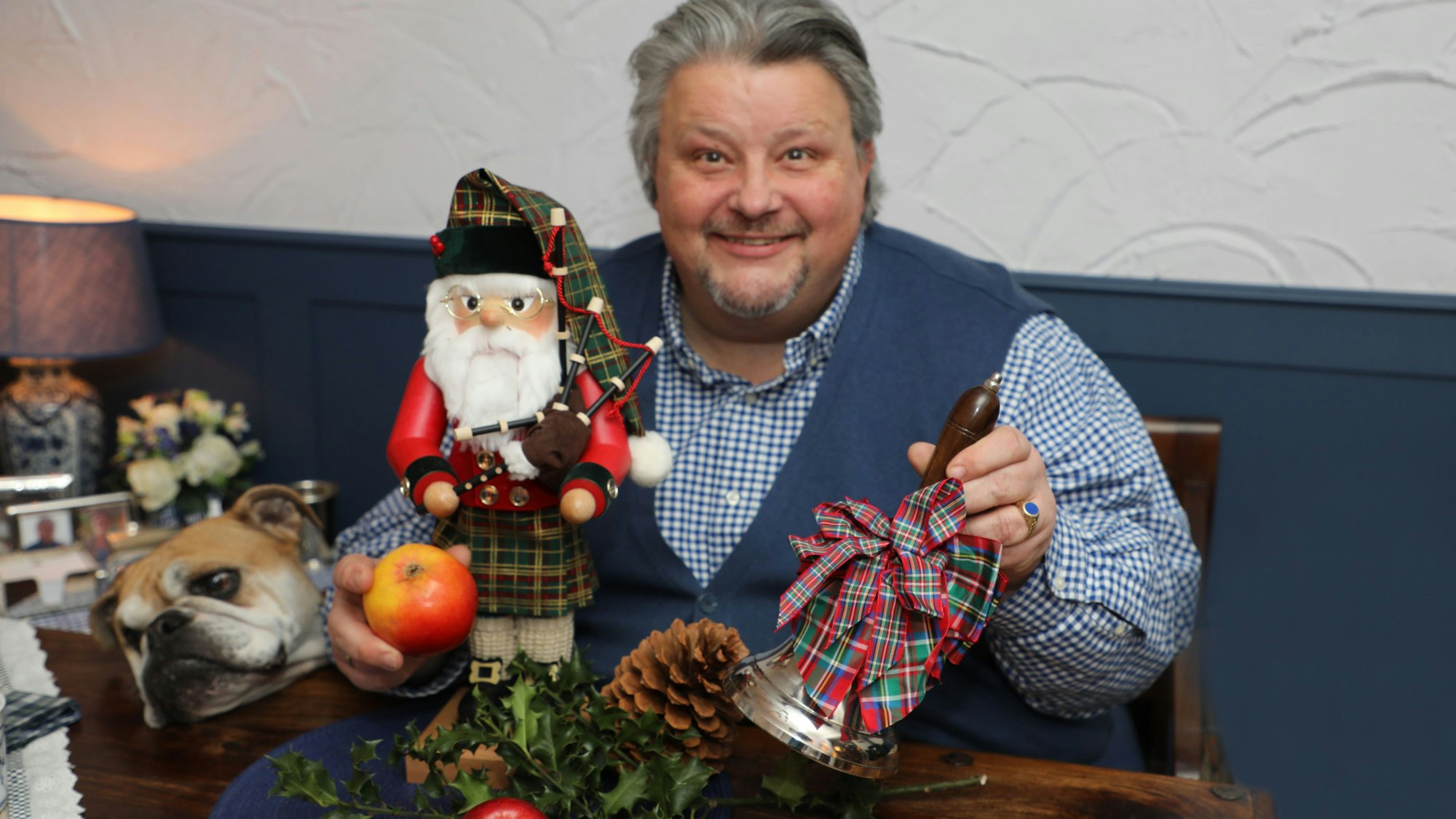 Karnevalist und Musiker Thomas Cüpper sitzt an einem Tisch und Weihnachtsdeko in der Hand. Seine Hündin Odette streckt ihren Kopf auf den Tisch.