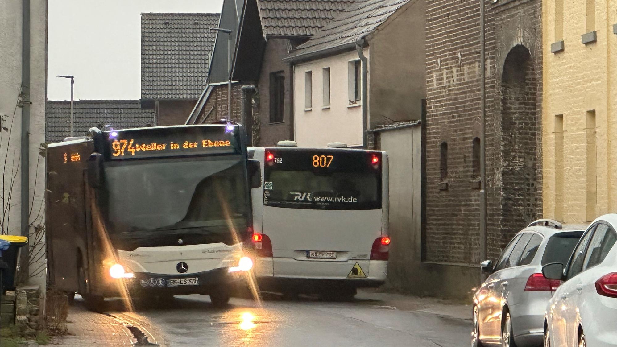 Zwei Busse fahren auf einer schmalen Straße aneinander vorbei.