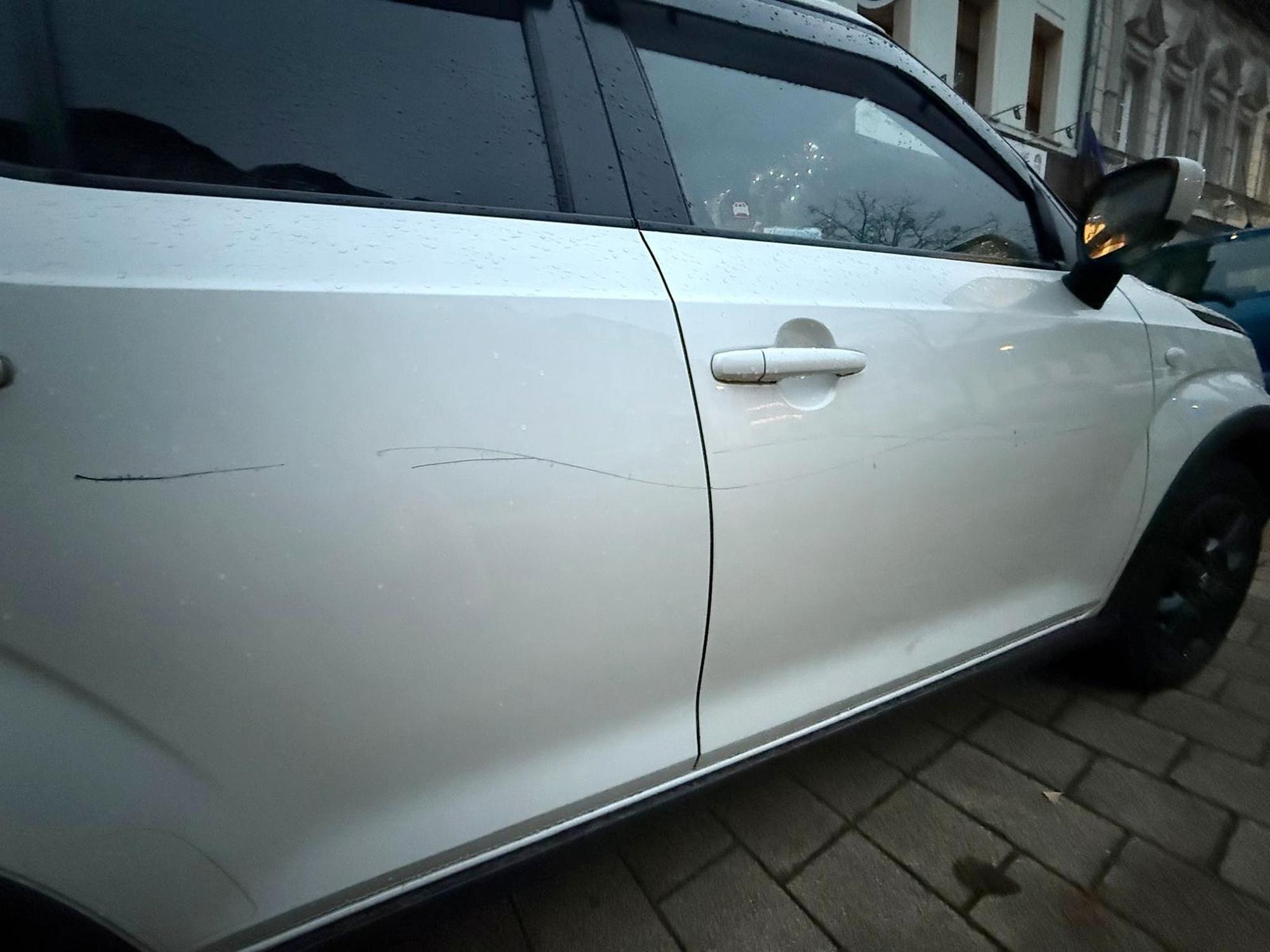 Das Bild zeigt ein weißes Auto mit einem langen Kratzer.