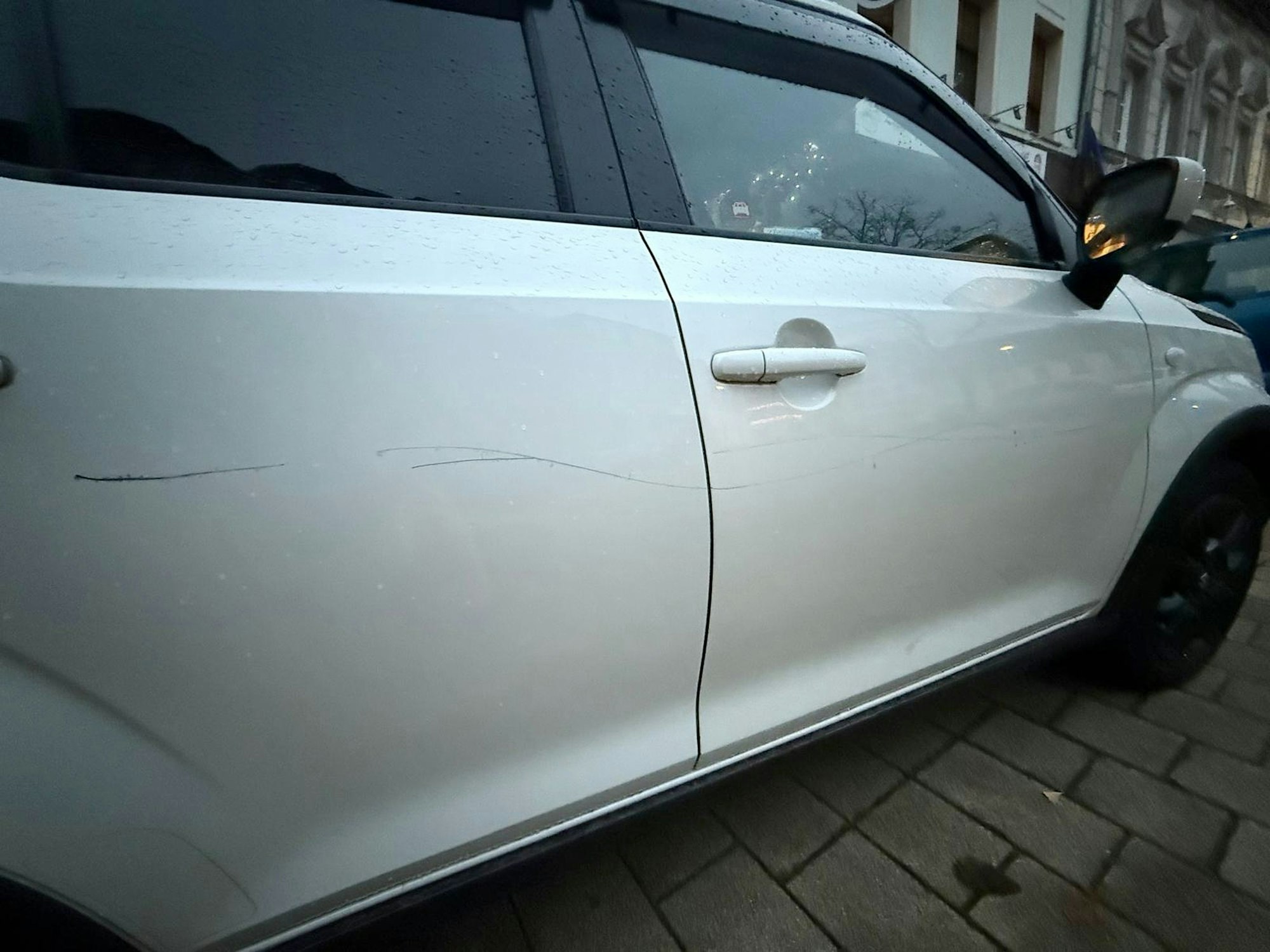 Das Bild zeigt ein weißes Auto mit einem langen Kratzer.