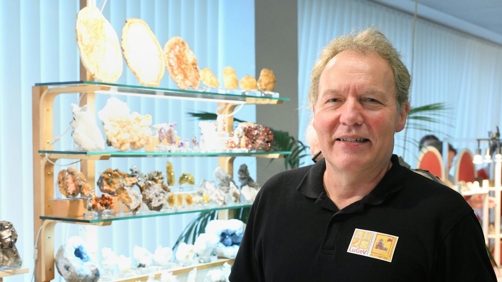 Diplom-Geologe Randolf Link steht vor einem Regal mit bunten Mineralien.