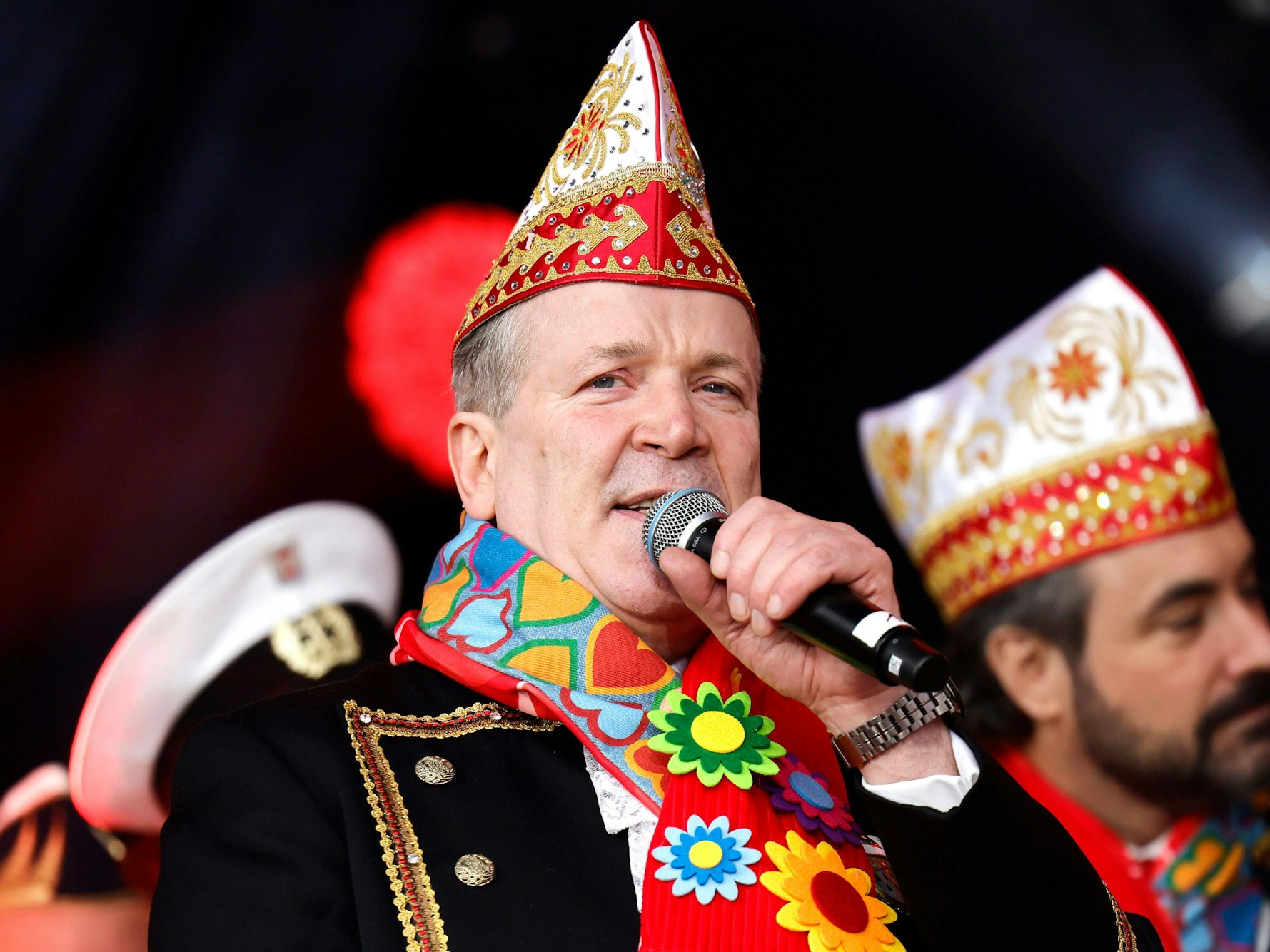 Christoph Kuckelkorn mit Narrrenkappe und Mikro in der Hand.