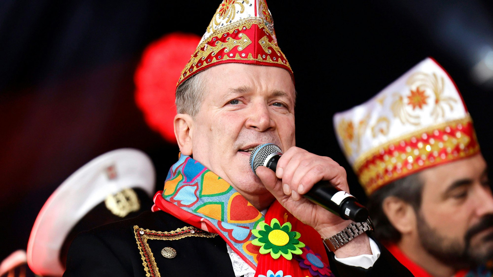 Christoph Kuckelkorn mit Narrrenkappe und Mikro in der Hand.