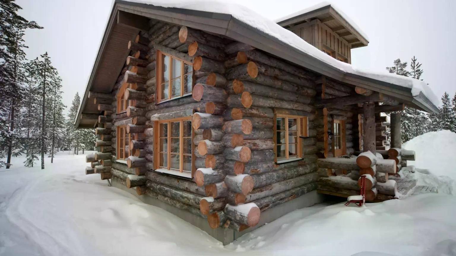 Das Bild zeigt eine gemütliche Hütte im verschneiten Winterwald in Finnisch-Lappland