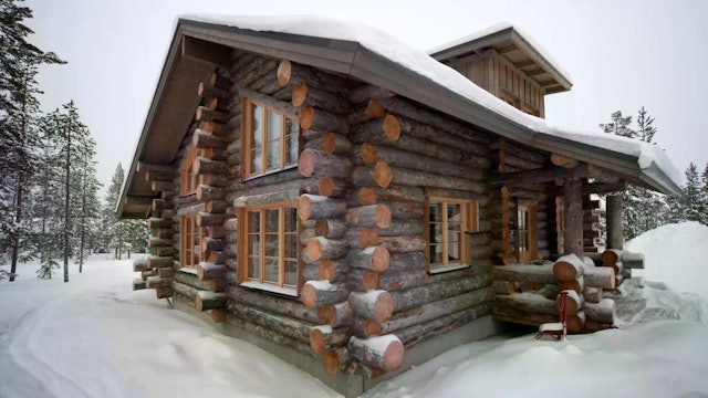 Das Bild zeigt eine gemütliche Hütte im verschneiten Winterwald in Finnisch-Lappland