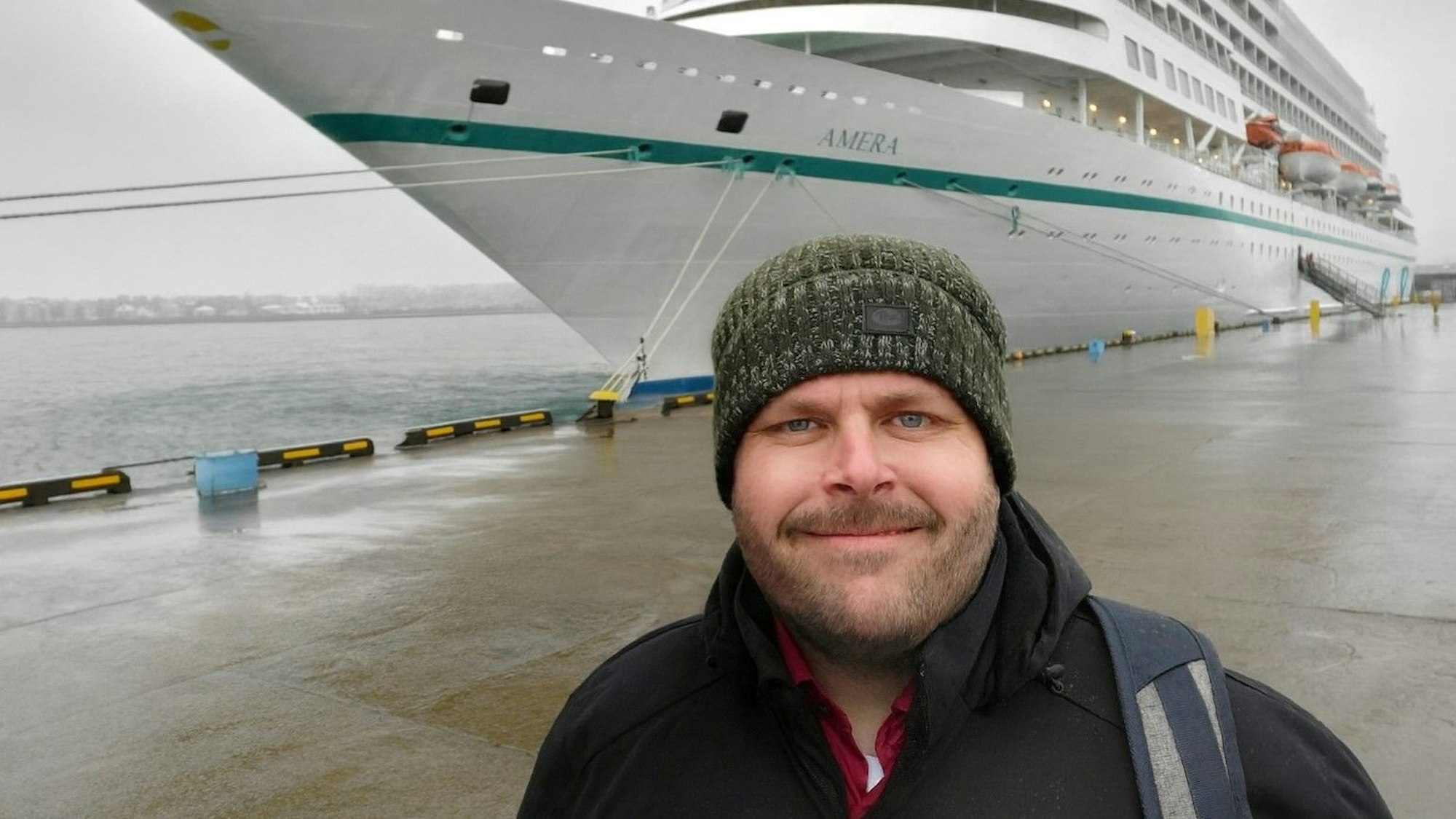 Ein Mann steht mit Mütze vor einem Kreuzfahrtschiff