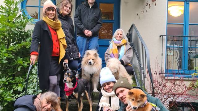 Einige Menschen und Hunde stehen und hocken auf einer Treppe vor einem Hauseingang.