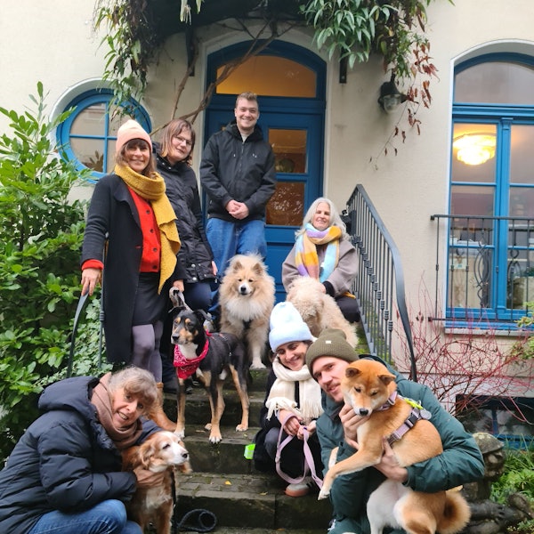 Einige Menschen und Hunde stehen und hocken auf einer Treppe vor einem Hauseingang.