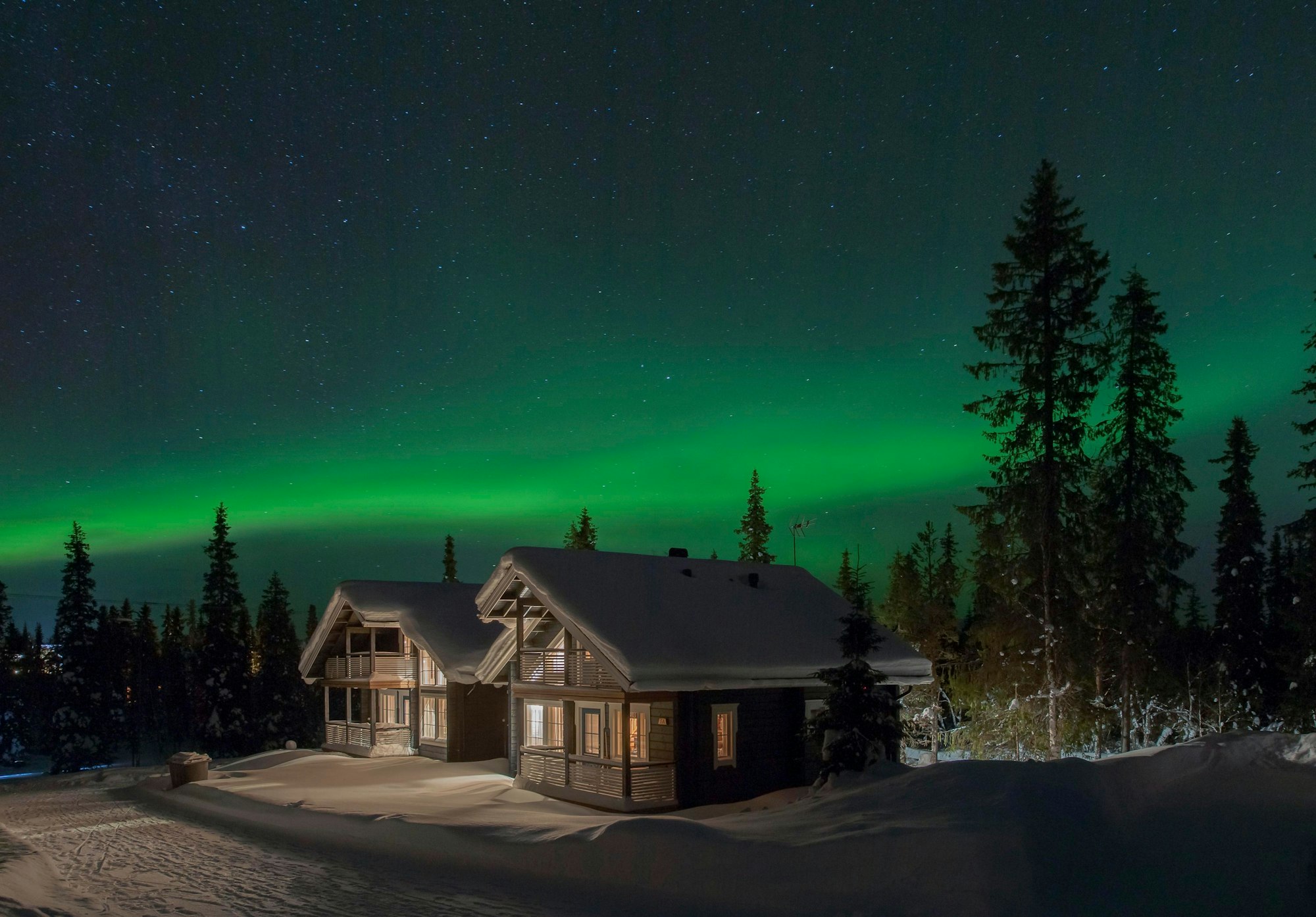 Das Bild zeigt eine Winterhütte in einer klaren Winternacht. Über der Blockhütte sind Polarlichter zu sehen.