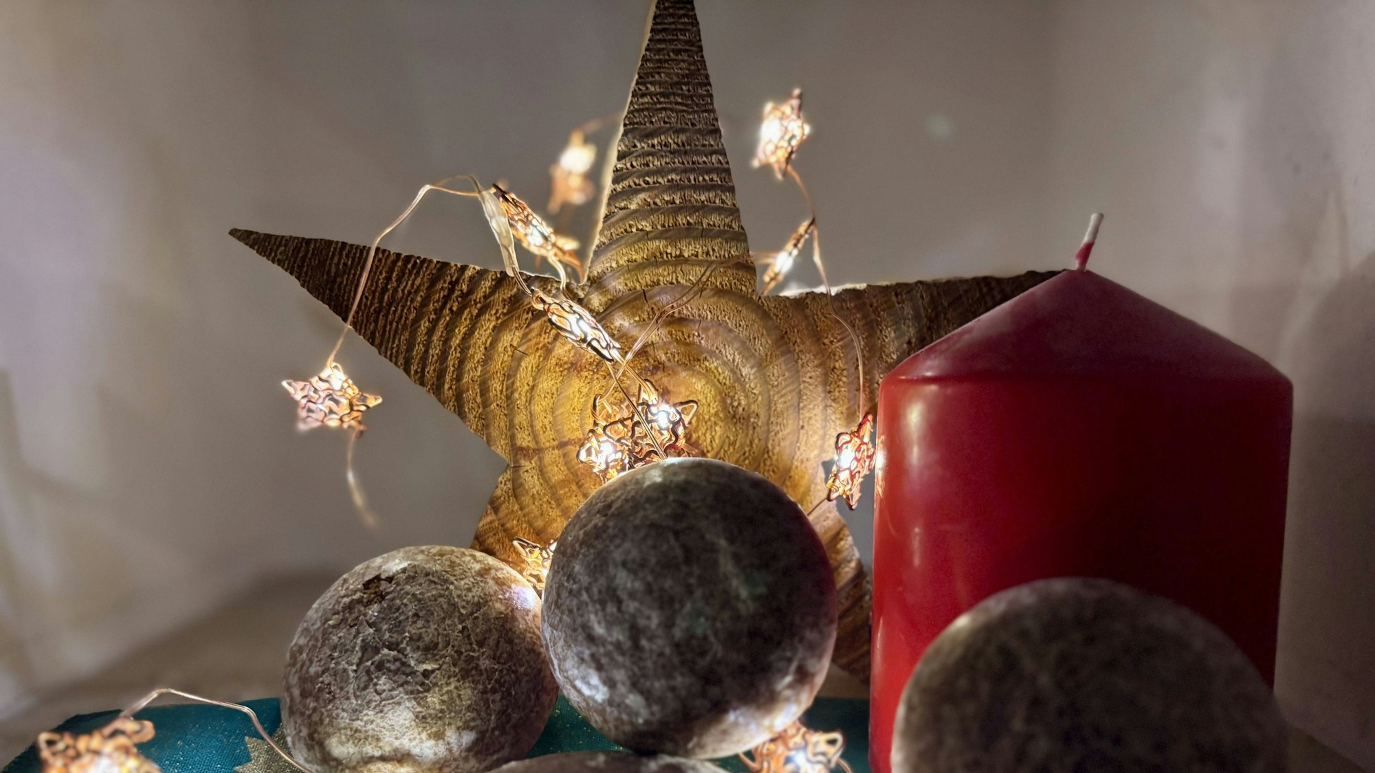 Ein beleuchteter Holzstern, davor eine rote Kerze und Gebäck aus Lebkuchen.