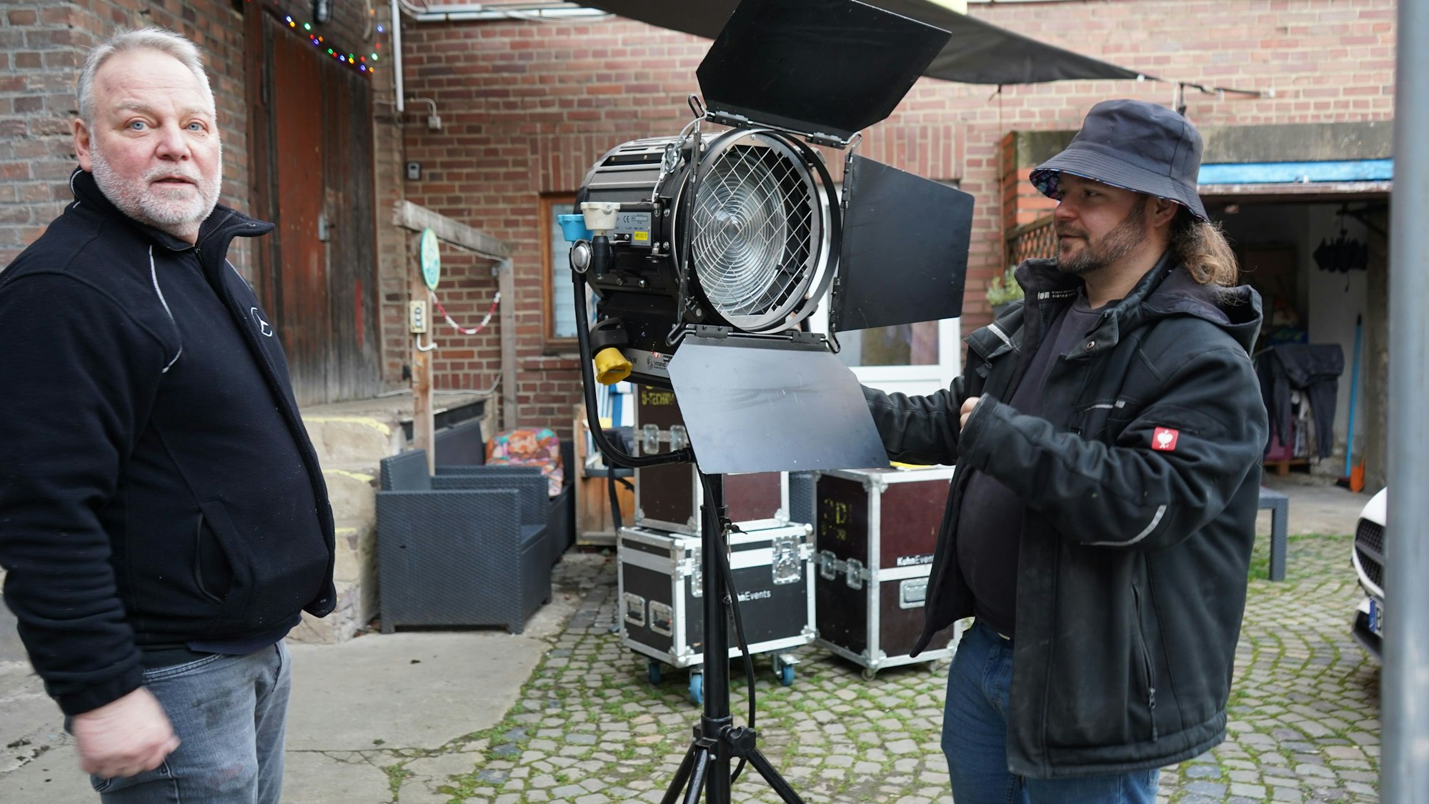 Das Foto zeigt zwei Männer, die einen Scheinwerfer aufbauen.