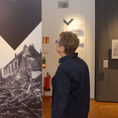 Eine Frau betrachtet ein großformatiges Foto, das die Zerstörung von Häusern in Euskirchen während des Zweiten Weltkrieges zeigt.
