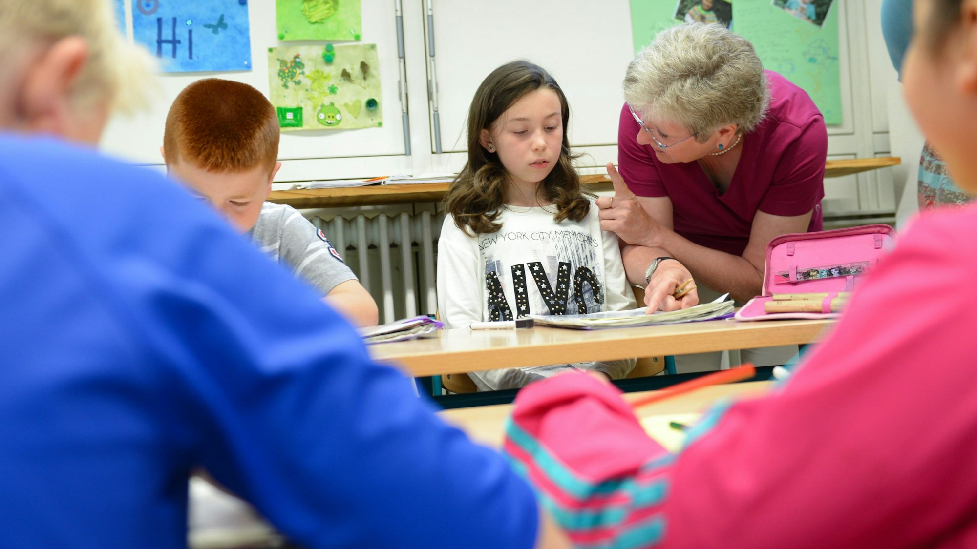 Eine Frau redet mit einem Mädchen, das an einem Schultisch sitzt.