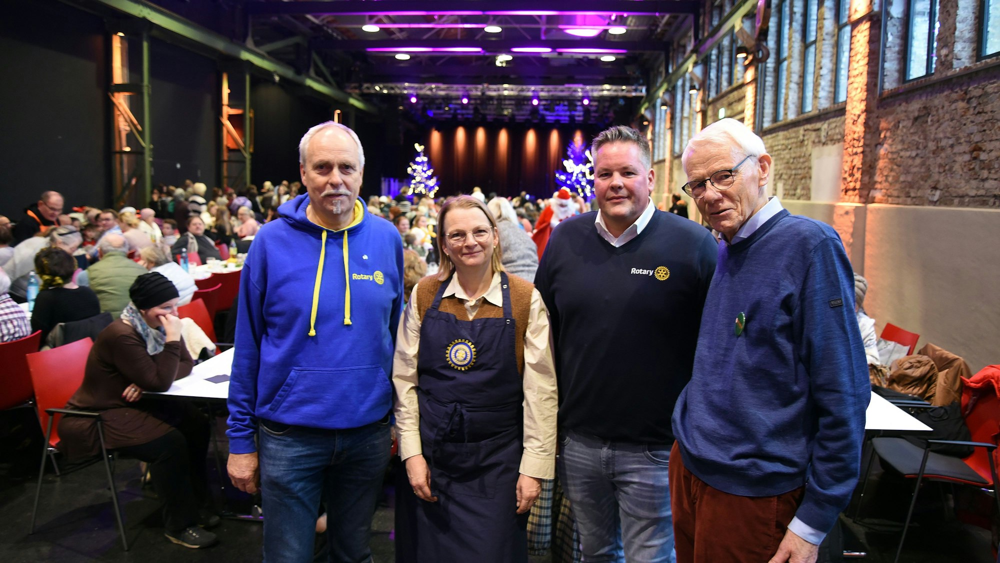 Vier Personen in einem Saal mit langen Tischen.