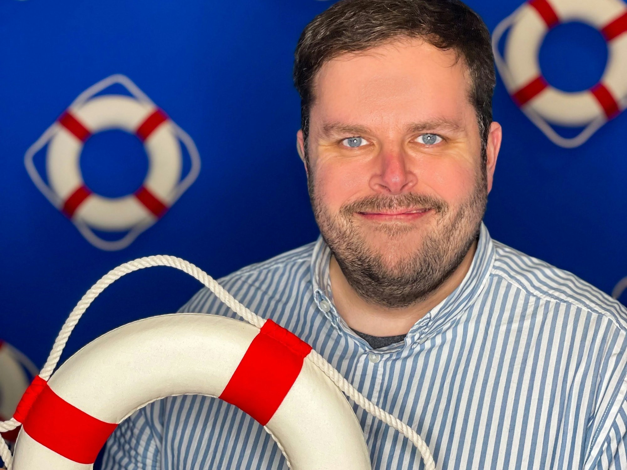 Ein Mann in blau-weißem Hemd hält einen Rettungsring in die Kamera.