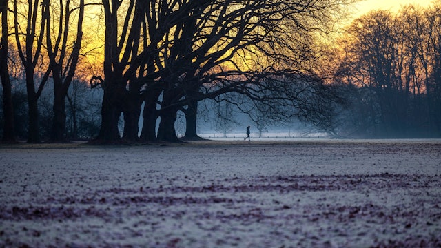 Ein Mann spaziert bei Sonnenaufgang im Winter durch einen Park in Köln. (Archivbild)