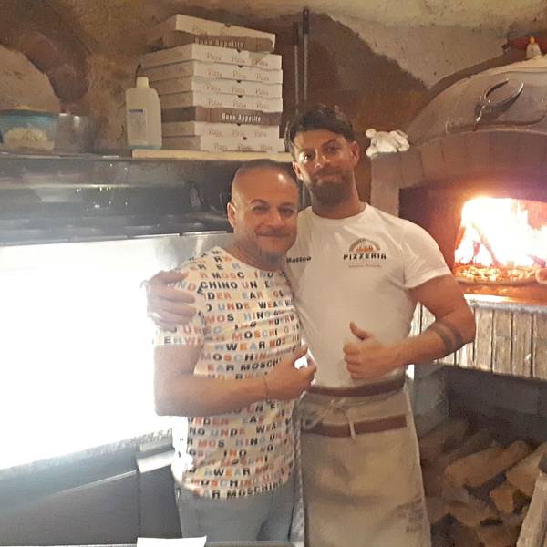 Zwei Männer stehen in einer Pizzeria vor dem großen Steinofen.
