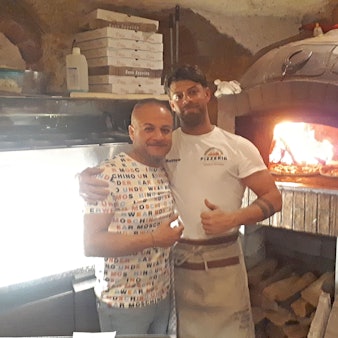 Zwei Männer stehen in einer Pizzeria vor dem großen Steinofen.