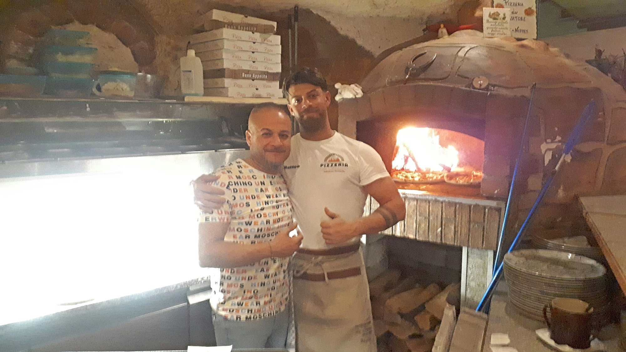 Zwei Männer stehen in einer Pizzeria vor dem großen Steinofen.