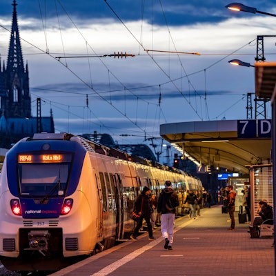 Das Bild zeigt einen Zug des Betreibers National Express im Bahnhof Köln-Deutz. Im Hintergrund ist der Kölner Dom zu sehen. Foto: IMAGO/Jochen Tack