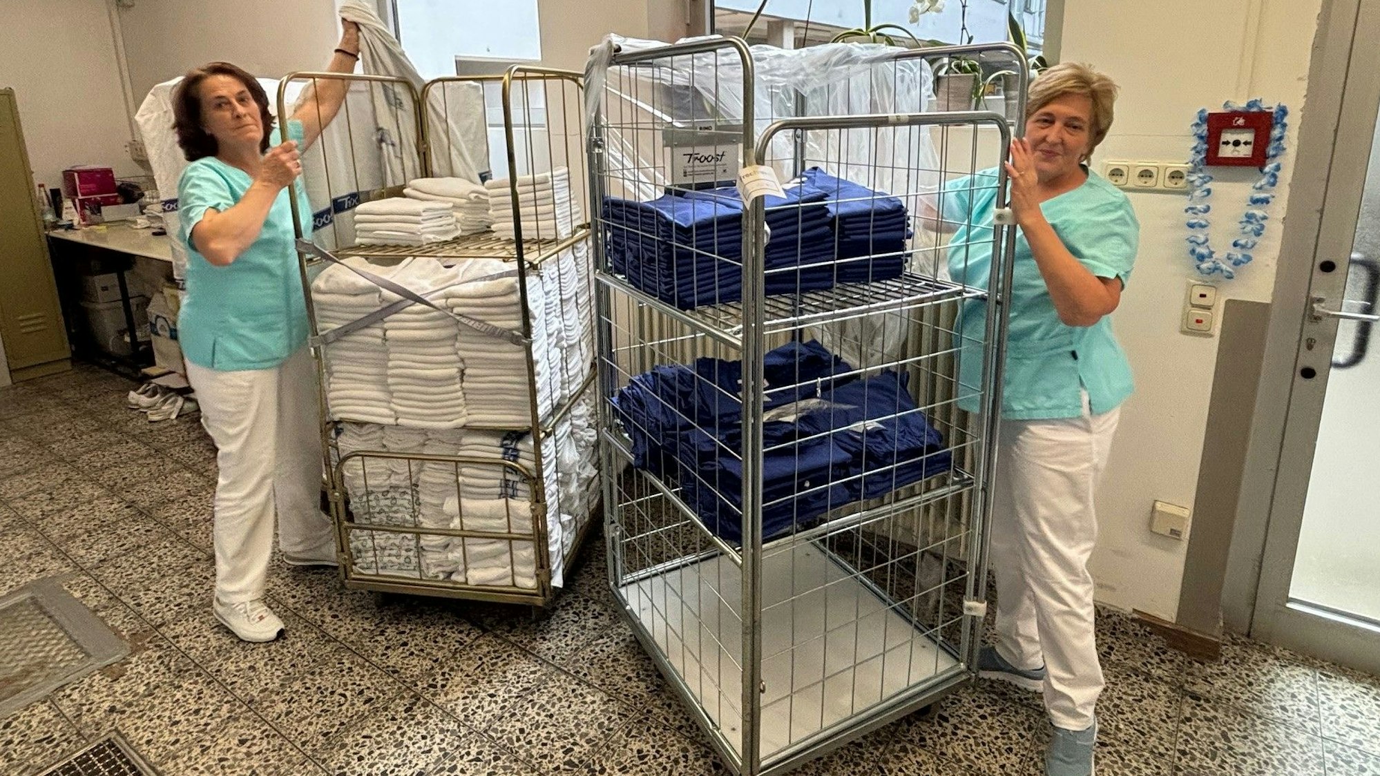 Auf dem Bild sind zwei Frauen mit zwei Rollwagen mit Wäsche zu sehen.