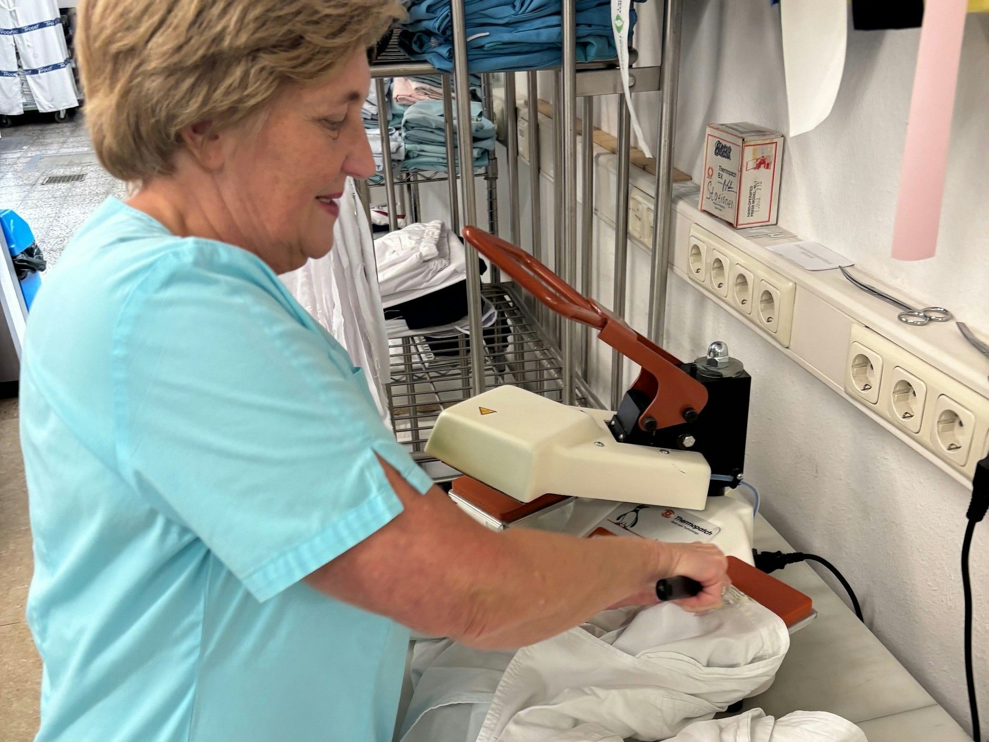 Auf dem Bild ist eine Frau mit einem Wäschestück an einem Spezialgerät zu sehen.