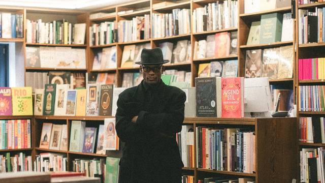 Das Bild zeigt den Künstler Don L. Gaspár Ali vor Bücherregalen in der Buchhandlung Franz Walther könig in Köln.