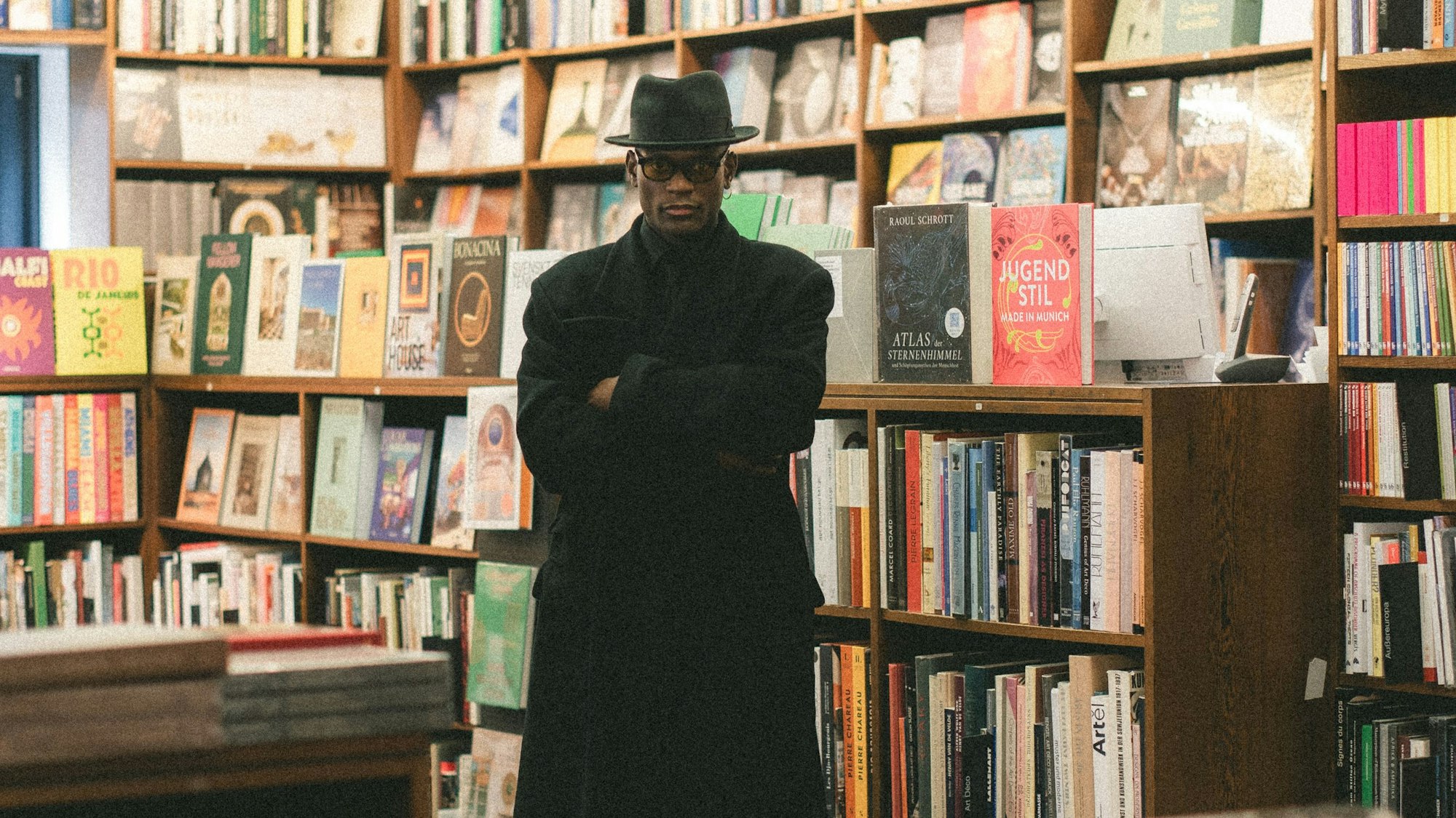 Das Bild zeigt den Künstler Don L. Gaspár Ali vor Bücherregalen in der Buchhandlung Franz Walther könig in Köln.