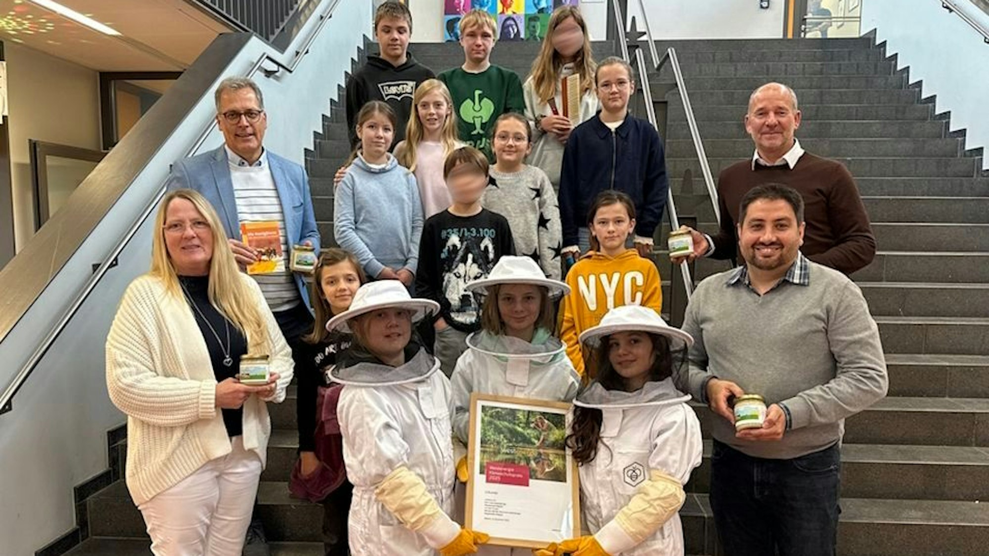 Eine Gruppe Kinder und einige Erwachsene haben sich auf einer Treppe zum Gruppenbild aufgestellt. Drei der Mädchen tragen Imkerkleidung.