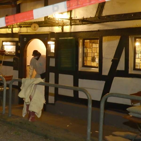 Ein Polizeiflatterband sperrt eine Gaststätte in Rösrath-Hoffnungsthal am Abend des 17. März 2025 ab. Ein Ermittler der Polizei steht in der Tür.